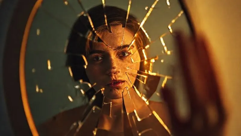A photorealistic image depicting fragmented reflections of a person in a broken mirror, symbolizing shattered self-perception and identity after trauma. The fragments are beginning to glow with a soft, warm light, hinting at healing. Professional photography, 8K, cinematic lighting, sharp focus, depth of field, shot on a high-end DSLR.